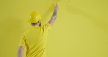 Sarı duvarın yanında boya silindirli genç bir adam var.