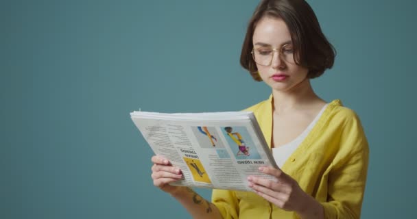 Mujer Joven Con Anteojos Leyendo Periódico Sobre Fondo Gris — Vídeos de Stock