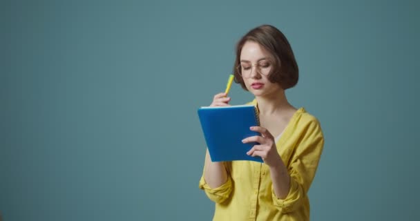 Mujer Joven Con Anteojos Escribiendo Algo Cuaderno Sobre Fondo Gris — Vídeos de Stock