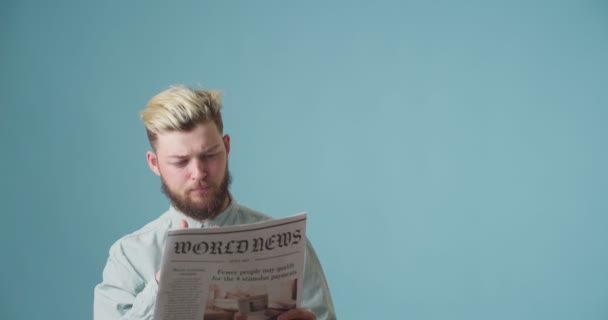 Emotionaler Junger Mann Liest Zeitung Auf Farbigem Hintergrund — Stockvideo