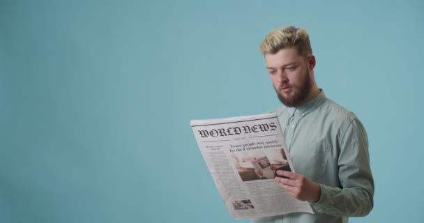 Emotionaler Junger Mann Liest Zeitung Auf Farbigem Hintergrund — Stockvideo