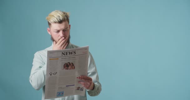 Эмоциональный Молодой Человек Читает Газету Цветном Фоне — стоковое видео