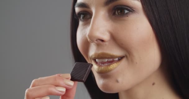 Hermosa Joven Con Maquillaje Inusual Comiendo Chocolate Dulce Sobre Fondo — Vídeos de Stock