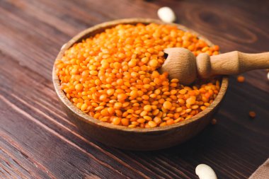 Ahşap arka planda çiğ mercimek ile kase ve kepçe, yakın plan