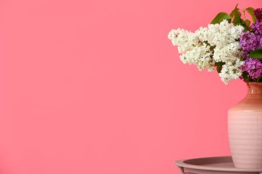 Renk duvarının yanındaki masada leylak çiçekli vazo.