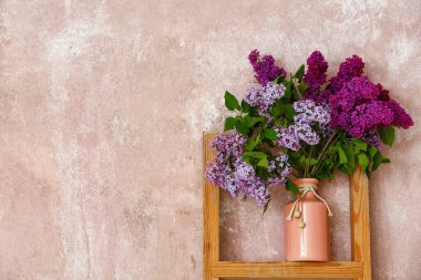 Renk duvarının yanındaki rafta leylak çiçekleri olan vazo.