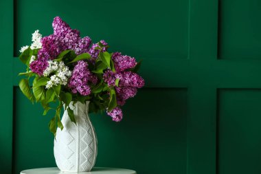Renk duvarının yanındaki masada leylak çiçekli vazo.