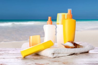 Tropikal tatil beldesindeki masada havluyla güneş kremi şişeleri.