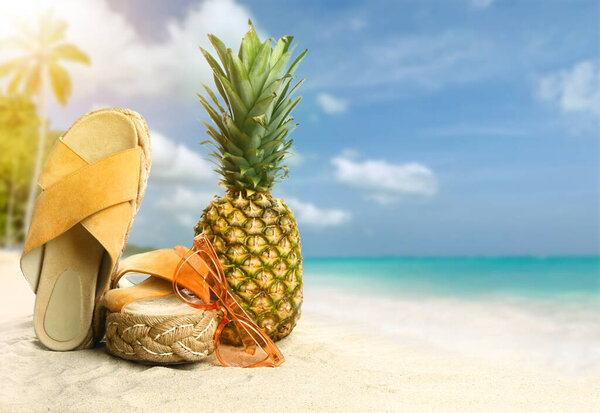 Stylish beach accessories with pineapple on sand at tropical resort