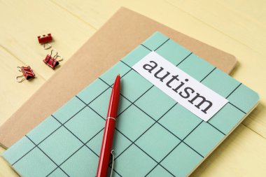 Kelime AUTISM ve renkli ahşap arkaplan üzerine kalem içeren defterler