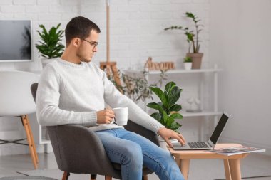 Genç adam evde dizüstü bilgisayar kullanıyor.