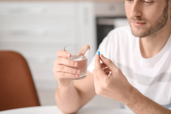 Красивый молодой человек, принимающий таблетки на кухне