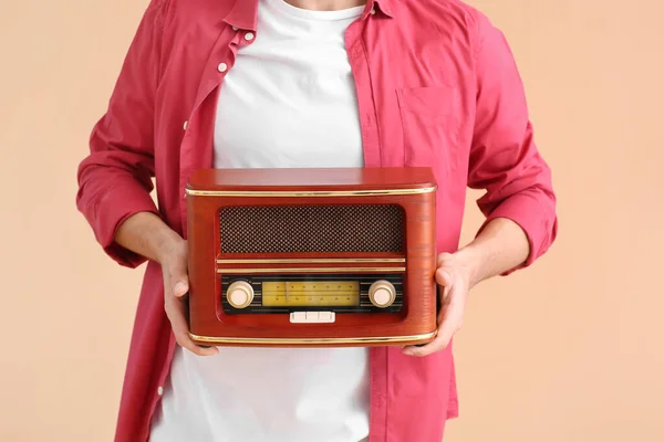 Young man with retro radio receiver on color background