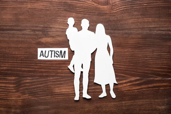 深色木制背景下的家庭形象和带有单词Autism的纸 — 图库照片