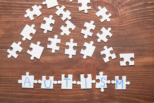 Word AUTISM made of puzzles on dark wooden background