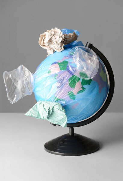 Творческая композиция с глобусом и мусором на сером фоне. Экологическая концепция, крупный план