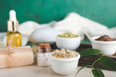 Kâselerde kuru kına tozu, arka planda gerekli yağ ve sabun şişesi, yakın plan.