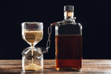 Masada bir şişe viski, kelepçe ve kum saati. Alkolizm kavramı