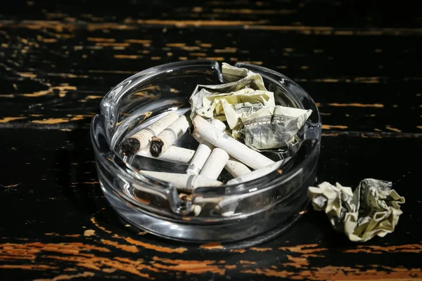 Bandeja Cinzas Com Cigarros Notas Amassadas Sobre Fundo Madeira Escura — Fotografia de Stock