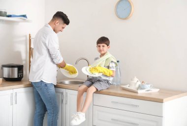 Baba oğul mutfakta bulaşık yıkıyorlar.