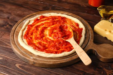 Lezzetli domates soslu pizza hamuru ve ahşap arka planda peynir.