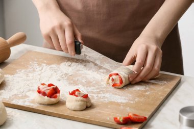 Kadın aşçı mutfak masasında çiğ hamur kesiyor, yakın plan.