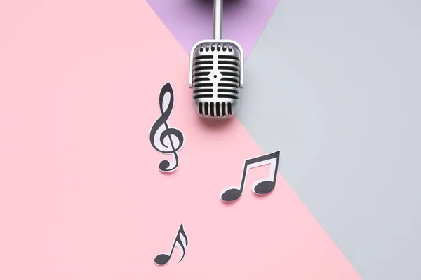 Modern microphone with music notes on color background