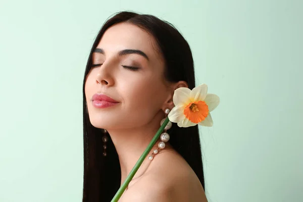 Beautiful young woman with narcissus on color background