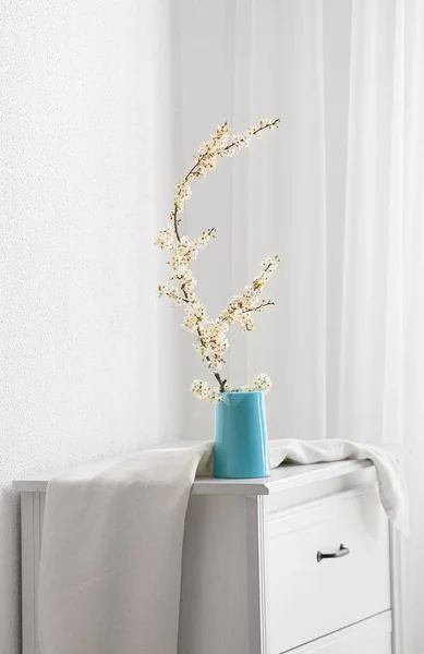 光の壁の近くのテーブルの上に美しい開花枝でジャグ — ストック写真