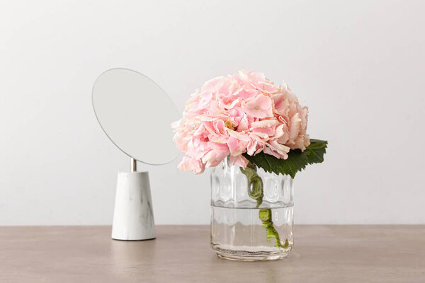 Vase with beautiful hydrangea flowers and mirror on table