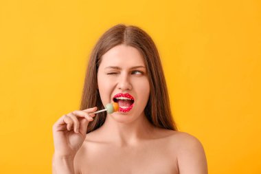 Yaratıcı makyajlı güzel genç bir kadın ve renkli arka planda tatlı bir lolipop.