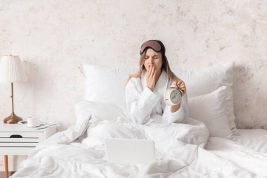 Yatak odasında çalar saati olan genç bir kadın.