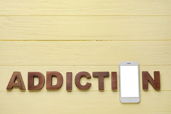 Mobile phone and word ADDICTION on wooden background