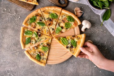 Kadın eli, arka planda lezzetli pizzadan bir dilim alıyor.