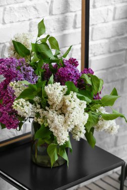 Tuğla duvarın yanındaki masada leylak çiçekli vazo