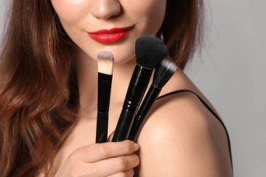 Gri arkaplanda makyaj fırçaları olan güzel bir genç kadın. Yakın plan.