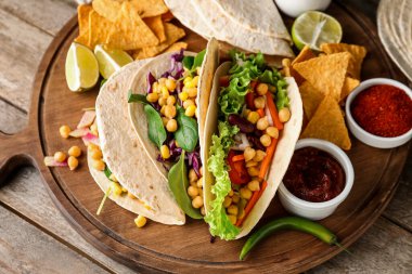 Lezzetli vejetaryen taco, nachos ve ahşap arka planda sos.