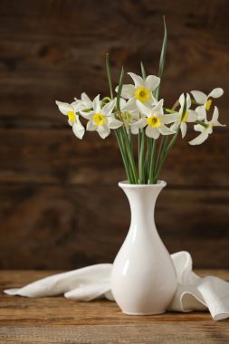 Ahşap zemin üzerinde güzel nergisler olan vazo.