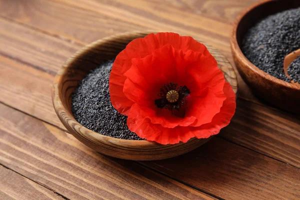 Bowls with poppy seeds and flower on wooden background