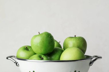 Açık arkaplanda taze yeşil elmaları olan Colander