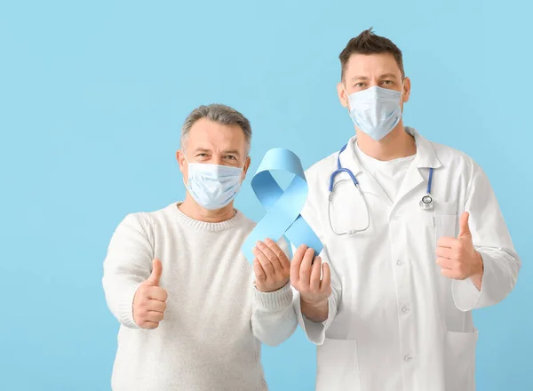 医師と青色のリボンを持つ成熟した男は 色の背景に親指アップジェスチャーを示しています 前立腺がんの認知概念 — ストック写真