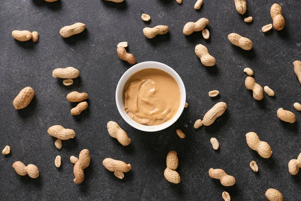 Bowl with tasty peanut butter and nuts on dark background