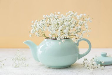 Renkli duvarın yanındaki masada güzel çigila çiçekleri olan çaydanlık, yakın plan.