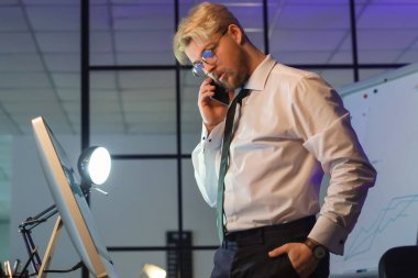 Geceleri ofiste cep telefonuyla konuşan yakışıklı bir adam.