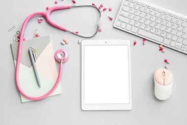 Steteskoplu tablet bilgisayar, gri arka planda doktor ilaçları ve aksesuarları.