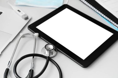 Steteskoplu tablet bilgisayar ve gri arka planda doktor aksesuarları.