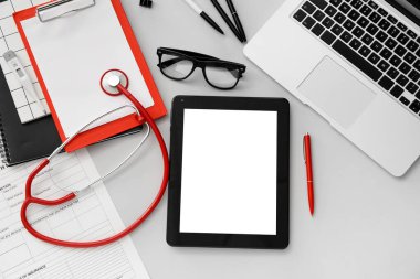 Steteskoplu tablet bilgisayar ve gri arka planda doktor aksesuarları.