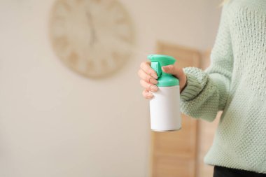 Evde oda spreyi olan genç bir kadın var.