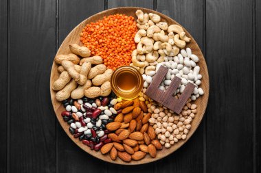 Koyu ahşap arka planda E vitamini bakımından zengin balık yağı ve farklı sağlıklı fındıklı tabaklar.