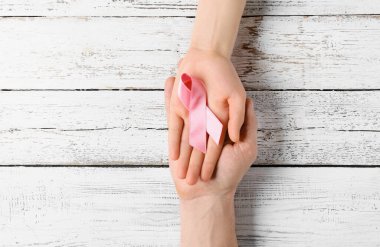 Hafif ahşap arka planda pembe kurdeleli eller. Göğüs kanseri kavramı